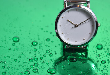 Women's watch on a green table with water drops.