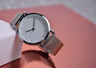 Women's watches lie near the box on a pink background.