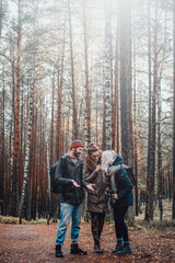Bearded guy and two beautiful girls talking and getting fun exploring autumn forest.