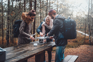 Cheerful company of three students a guy and two girls tuning quadcopter at table in shiny and...