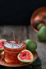 Fig jam in glass jar on copper Turkish platter, half fresh fig next to it and fruit in the background. close-up, preparation of dessert from autumn fruits, dark wooden background, copy space