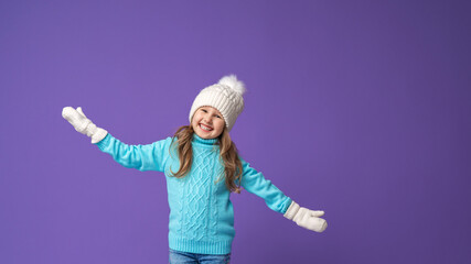 Happy little girl in a knitted sweater hat and mittens smiling on a lilac background