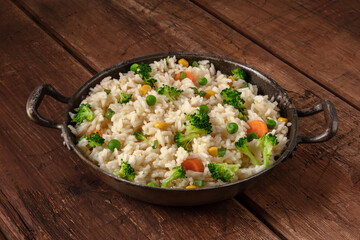 Vegetable rice with broccoli, carrots and green peas, in a frying pan on a dark rustic wooden background