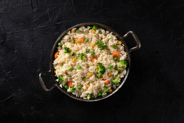 Vegetable rice, shot from the top on a black background. Basmati with broccoli, carrots and green peas, easy recipe