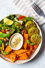Falafel salad bowl. Vegan lunch plate - baked chickpea cutlets with baked sweet potatoes and vegetable salad in a white plate, top view.