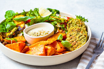 Falafel salad bowl. Vegan lunch plate - baked chickpea cutlets with baked sweet potatoes and vegetable salad in a white plate.