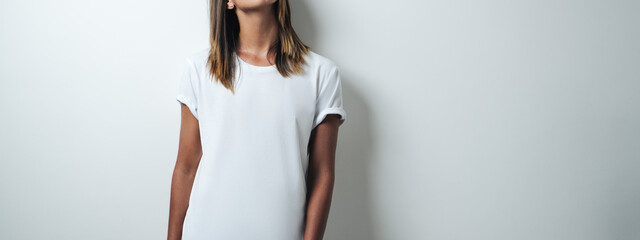Handsome caucasian girl in white blank t-shirt, empty wall, studio portrait. Wide screen, panoramic