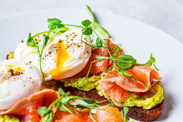 Toast with salmon, poached egg and avocado on white plate. Poached egg with salmon and guacamole on rye bread.