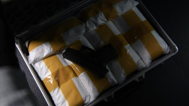 A hand opening the briefcase full of narcotic drugs with a gun
