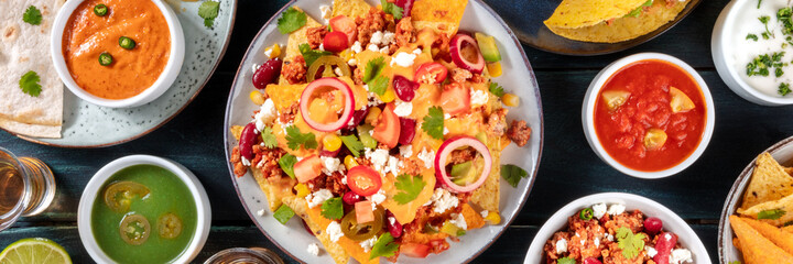 Mexican food panorama. Nachos with beef and cheese sauce and various dips, shot from above on a dark blue wooden background