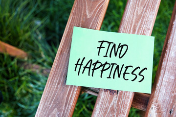 Find happiness inspirational life quote text written on paper on a wooden bench in a garden.