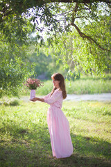 beautiful girl in a pink dress walks with a bouquet of pink flowers, a photo session in a fairy-tale style at sunset