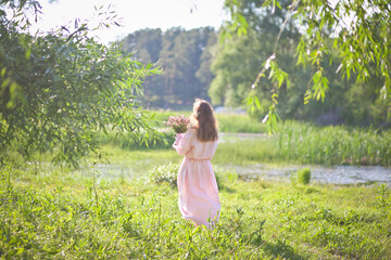 Naklejka na ściany i meble beautiful girl in a pink dress walks with a bouquet of pink flowers, a photo session in a fairy-tale style at sunset