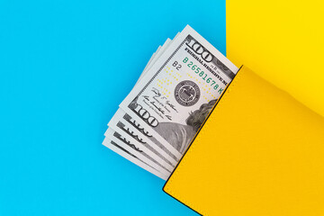 Close-up of yellow wallet with 100 dollar banknotes on a colored background