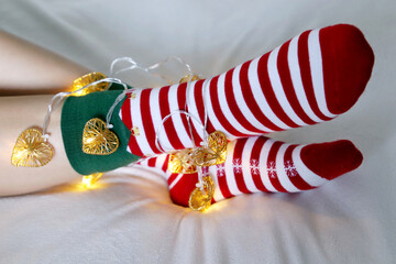Female legs in Christmas socks with garland and festive lights in heart shape. Concept of romantic...