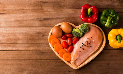 Top view of Raw chicken breasts fillets no boneless with spices rosemary, carrot, and eggs in heart plate wood on wooden background, Healthy food day concept