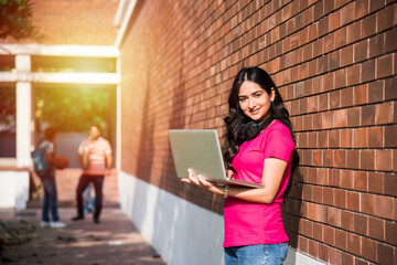 One Indian college student with laptop or book in focus with friends in the background out of focus