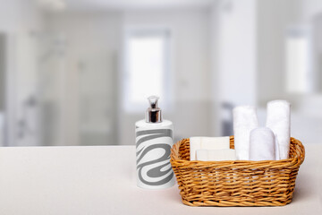 Fototapeta na wymiar Basket with bath accessories such as soap bars, Cream and cosmetic tissues for body care on a white table over blurred bathroom background with copy space. For your product display montage.