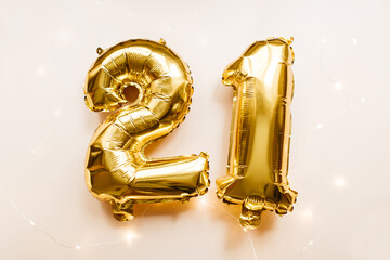 Gold foil balloons number 21 twenty one on beige background. Merry Christmas, happy new year 2021, birthday concept. Party decoration. Flat lay, top view.