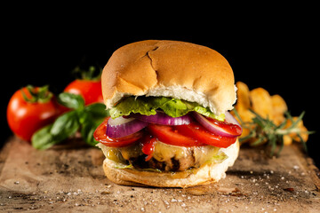 Closeup of a delicious fresh home made hamburger with lettuce, cheese, tomato, red onion on a rustic wooden board.