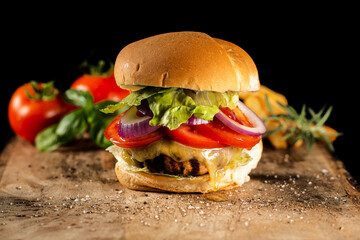 Closeup of a delicious fresh home made hamburger with lettuce, cheese, tomato, red onion on a rustic wooden board.