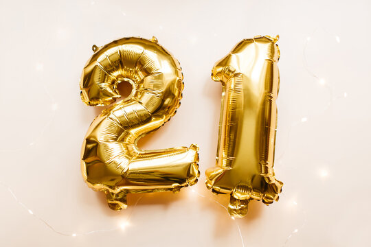 Gold foil balloons number 21 twenty one on beige background. Merry Christmas, happy new year 2021, birthday concept. Party decoration. Flat lay, top view.