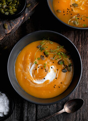 Bowl of yellow pumpkin soup with green leaf at the wooden table background. Top view