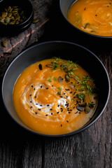 Bowl of yellow pumpkin soup with green leaf at the wooden table background. Top view