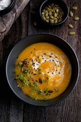 Bowl of yellow pumpkin soup with green leaf at the wooden table background. Top view