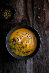 Bowl of yellow pumpkin soup with green leaf at the wooden table background. Top view