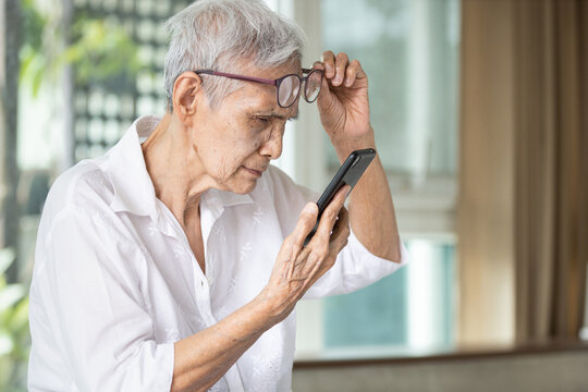Asian senior woman with eye glasses,try to read messages,gaze at the small text on mobile phone,age related macular degeneration,blurred vision,poor eyesight problems,eye disease of the old elderly.