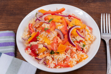 Traditional Mediterranean salad of couscous, tomato, pepper and onion in a plate on a wooden table, close-up - Moroccan and Algerian cuisine