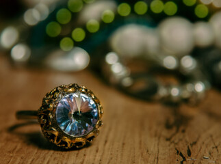 Fototapeta premium Glittering blue-turquoise colored, big ring on brown wooden table top with colorful bokeh background