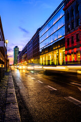 Fototapeta na wymiar Long exposure cityscape of street in central district in Berlin, Germany during sunset before dusk. Blurry cars passing by and leave the light trails. Modern and old architecture of European capital.