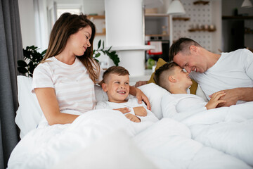 Obraz premium Young family enjoying in bed. Happy parents with sons relaxing in bed