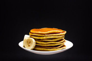 White plate on black background with pancakes and banana slices