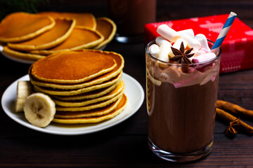 Pancakes with banana, maple syrup and a glass of hot chocolate with marshmallows and a drinking straw