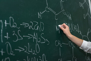 female hand draws chemical equations on a blackboard