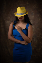 Studio portrait of an young Indian girl in blue western dress and yellow hat in front of textured background. Fashion portrait photography