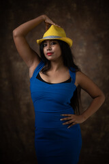 Naklejka premium Studio portrait of an young Indian girl in blue western dress and yellow hat in front of textured background. Fashion portrait photography