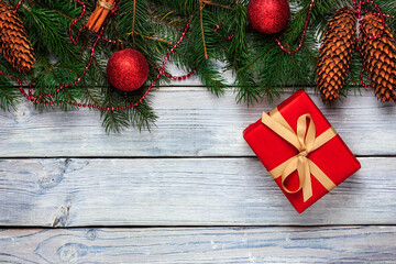Christmas gift with fir branches, pine cones, cinnamon sticks and Christmas decorations on a white wooden background. Top view, frame for text