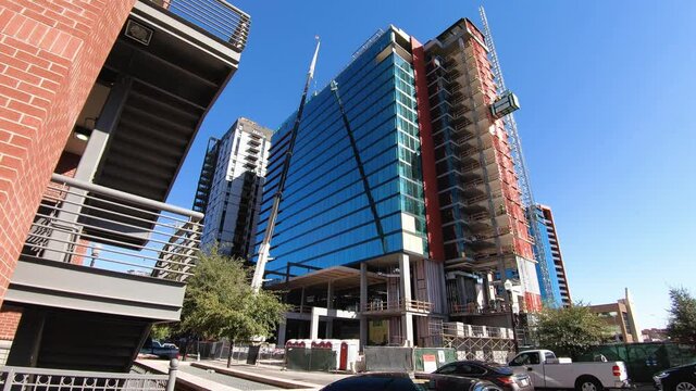 A busy construction site of a crane, elevator, workers, and traffic prepares a new glass and steel highrise to join the Tempe, Arizona skyline.