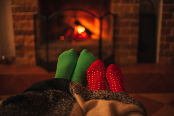 Man and woman, couple in love wearing green and red socks sitting near fireplace, hugging and wrapping in a woolen blanket.