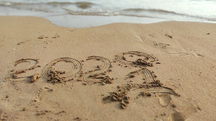 New Year 2021 and wave erasing 2020 year written in the sand