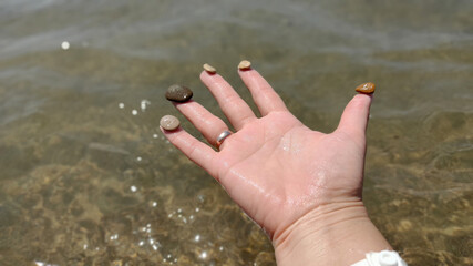 female hands holding sea pebbles on background of sea water
