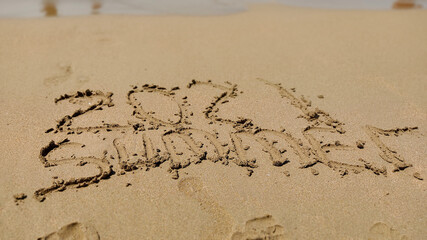 word handwritten summer 2021 on yellow sandy beach