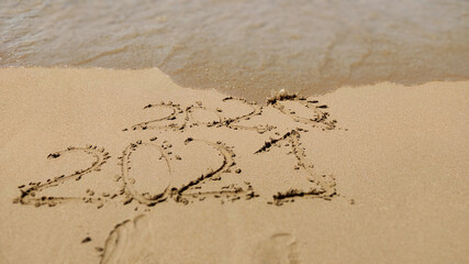 New Year 2021 and wave erasing 2020 year written in the sand