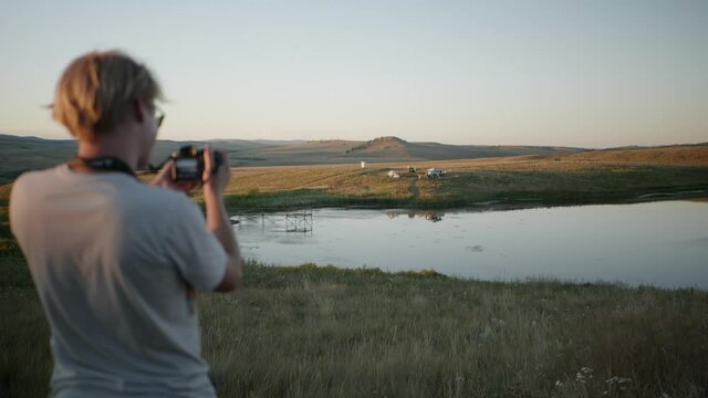 Man with camera takes pictures of beautiful prairie landscape with lake