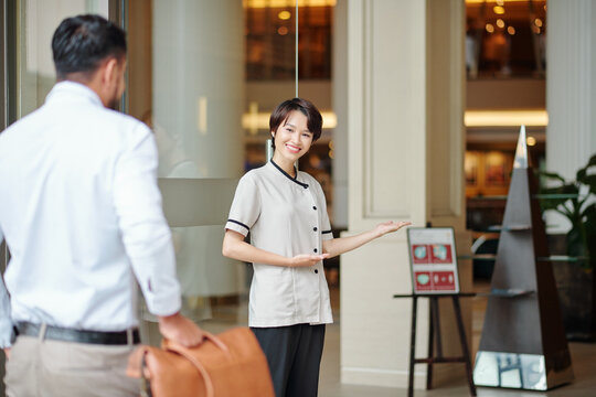Smiling hospitable consierge welcoming guest at doors of fancy hotel