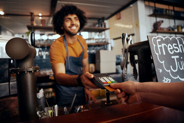 Waiter holding credit card swipe machine while customer typing code in modern cafe